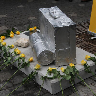 Kofferdenkmal am Flörsheimer Bahnhof. Am Tag der Einweihung (28. November 2021) haben Schüler des Graf-Stauffenberg-Gymnasiums gelbe Rosen am Denkmal abgelegt.